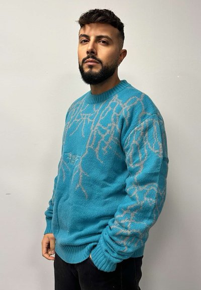 Maglione turchese a maglia con un design testurizzato che presenta motivi beige chiaro e maniche lunghe. Vestibilità rilassata con scollatura rotonda.