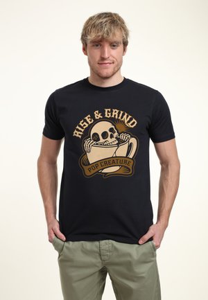 Schwarzes Baumwoll-T-Shirt mit einem grafischen Design eines Schädels in einer Kaffeetasse und dem Text "Rise & Grind" in Gold und Beige. Einfacher Rundhalsausschnitt.