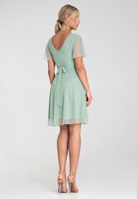 Mintgrünes Kleid mit kurzen durchsichtigen Ärmeln, V-Ausschnitt, Taillenzug und einem schwingenden Rock. Getragen mit silbernen Riemchen heels.