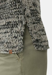 Pull en tricot avec un motif texturé en noir et crème, présentant une fente sur le côté et une petite étiquette en cuir à l'ourlet.