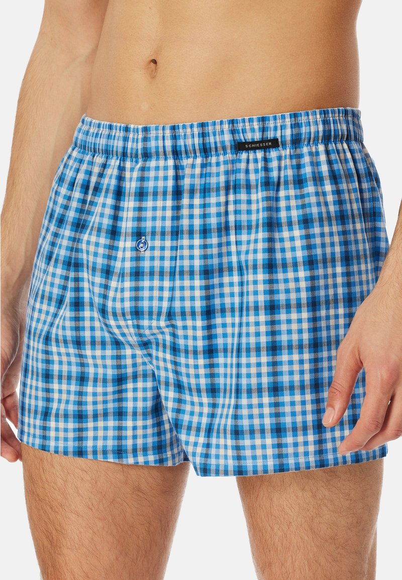 Blauwe en witte geruite boxershorts met een elastische tailleband en een zwart label. Materiaal is lichtgewicht stof met een subtiel patroon.