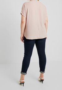 Blusa corta a maniche corte di un rosa chiaro con vestibilità rilassata, abbinata a jeans blu scuro con risvolto e scarpe bianche con tacco alto.