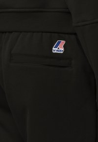 Pantaloni della tuta neri con tasca laterale e un piccolo logo K-Way colorato con accenti rossi, blu e bianchi. Tessuto morbido.