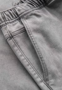 Gros plan sur un pantalon en tissu gris avec une taille élastique et une poche latérale avec des coutures visibles.