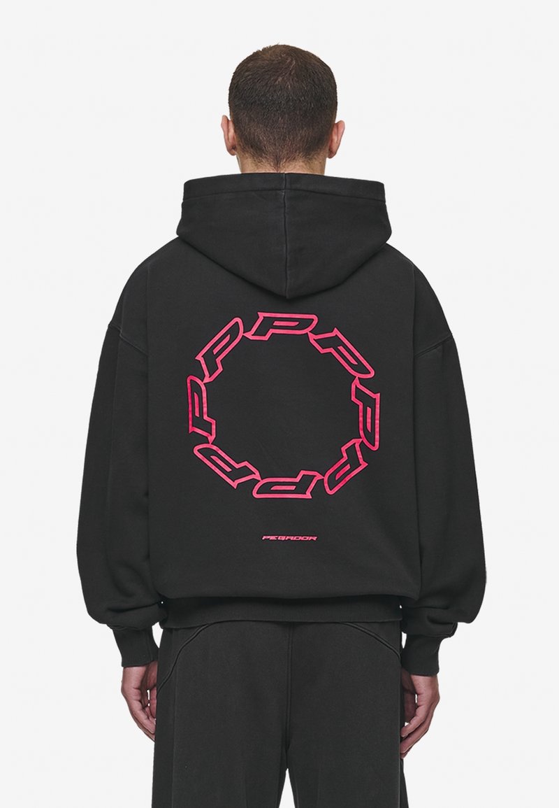 Sweat à capuche noir avec un grand motif circulaire rose vif dans le dos. Présente une coupe ample, une capuche et des poignets côtelés.