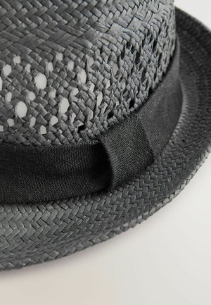 Fekete szőtt szalma kalap széles karimával, amelynek alján egy szilárd fekete szövet sáv található. Nyitott szövésű minta a korona közelében.