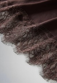 Tmavě hnědá tkanina s jemnou krajkou s květinovým vzorem, zahrnující jemnou síťovinu a jemné třásně na okrajích.