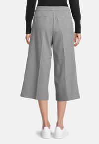 Osoba v černobílých kostkovaných širokých kalhotách ke kotníkům se zadními kapsami a bílými teniskami, zachycena zezadu.