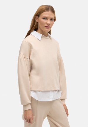 Sudadera beige con cuello redondo, mangas abullonadas y un cuello de camisa blanco insertado. Material suave, diseño corto y puños ajustados.