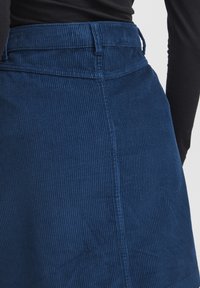 Donkerblauwe corduroy rok met verticale ribbelstructuur, met een hoge taille en stikdetails. Zichtbare tailleband en zijnaad.