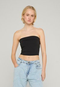 Top negru fără bretele, cu un design mulat, realizat dintr-un material neted. Asorat cu blugi din denim ușor albastri, cu talie înaltă și buzunare.