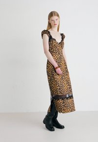 Robe à imprimé léopard avec un décolleté plongeant, des accents en dentelle et une fente sur le côté, fabriquée en tissu léger. Portée avec des bottes noires jusqu'aux genoux.