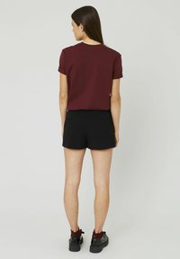 T-shirt marron à manches courtes associé à un short noir. La tenue présente un design simple avec des manches retroussées et une texture lisse.