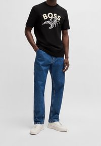 Svart bomullströja med en hummergrafik och ordet "BOSS" i krämfärg. Kombineras med blå denimbyxor och vita sneakers.