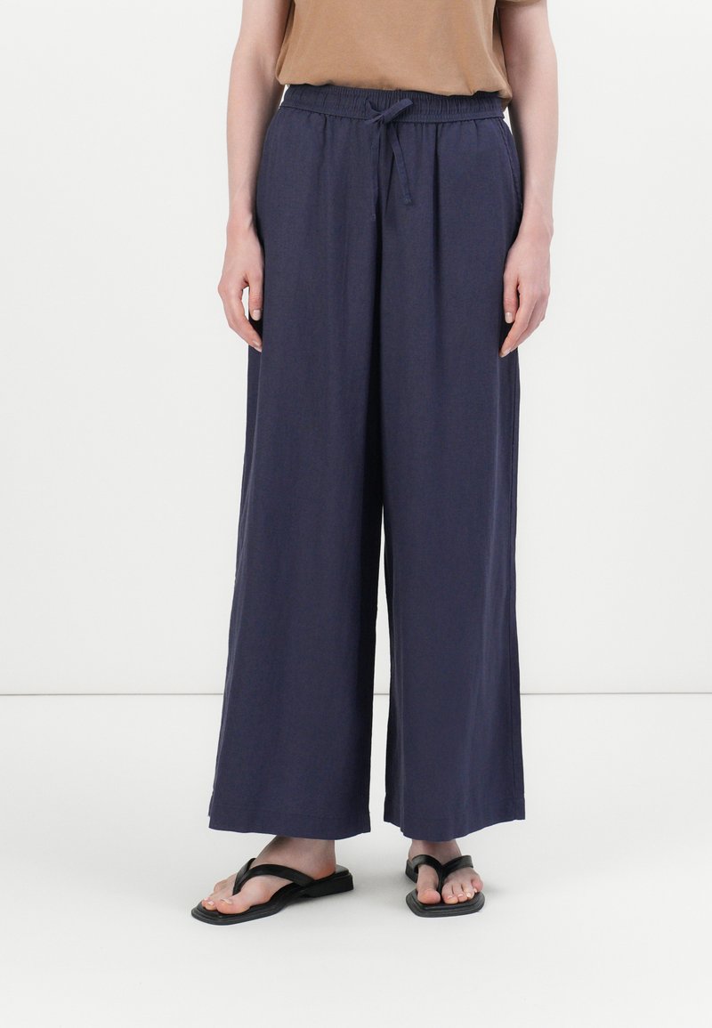 Navy wijde broek van lichtgewicht stof met een elastische tailleband en trekkoord, gecombineerd met zwarte slippers.