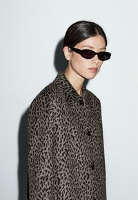 Leopard print coat in gray and black fabric, featuring a collared neckline and black button closures. Worn with slim black sunglasses.