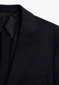 Blazer azul marino con solapas estructuradas, un bolsillo en el pecho y una textura de tela suave. Forro de satén visible en el cuello.