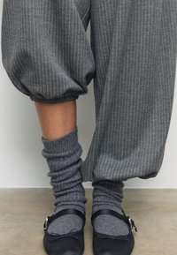 Sive prugaste hlače s naboranim manžetama, uparene s opuštenim sivim čarapama i crnim balerinama s detaljem mašne i kopče.