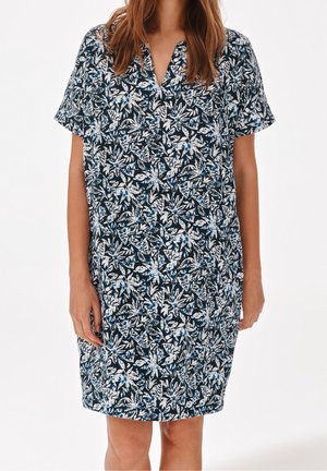 Frau trägt ein knielanges Kleid mit kurzen Ärmeln, marineblauem, weißem und blauem Blumenmuster sowie einem V-Ausschnitt.