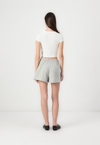 Grå korte joggebukser med elastisk midje, kombinert med en hvit tettsittende, rillede croppetopp, sett fra baksiden. Svarte sko fullfører antrekket.