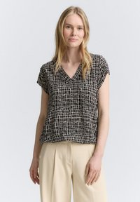Kurzärmlige Bluse mit schwarz-weißen Mustern und V-Ausschnitt, mit einem karierten Design aus gewebtem Stoff, kombiniert mit hellbeigen Hosen.