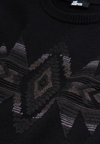 Pull en maille noir avec un motif géométrique gris et foncé en losange et triangle sur la poitrine et un col rond côtelé.