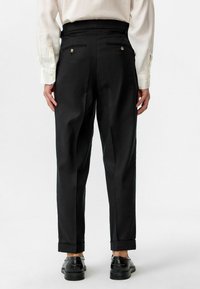 Zwarte broek met een rechte snit, voorzien van twee achterzakken met gouden knopen, opgestikte boorden en een gladde textuur.