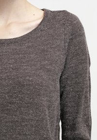 Grå stickad tröja med rund halsringning och långa ärmar, med en texturerad yta och en mjuk, lurvig finish.