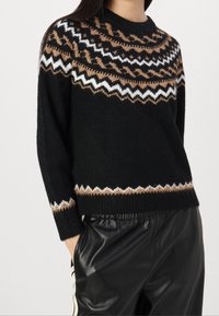 Pull en maille noire avec un large col rond, présentant un motif géométrique en marron, blanc et crème autour des épaules et de l'ourlet.