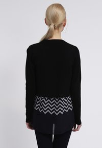 Black cropped sweater with long sleeves, layered over a gray and navy chevron-patterned top. Smooth texture, minimalist design.