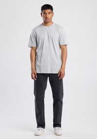 Graues T-Shirt mit Rundhalsausschnitt und kurzen Ärmeln, kombiniert mit dunkelgrauen Jeans und weißen Sneakern. Einfaches, lässiges Design ohne sichtbare Muster.