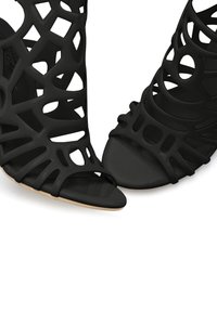 Schwarze, offene High-Heelsandaletten mit Ausschnitten aus glänzendem Material, mit strukturierter Oberfläche und geschwungenem Design.