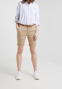 Světlemodrá a bílá pruhovaná košile na knoflíky, světle hnědé šortky po kolena, hnědý opasek a bílé tenisky. Jednoduchý design, neformální vzhled.