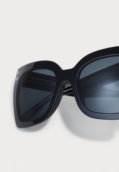 Black oversized sunglasses with rounded edges, dark lenses, and three small studs on each side. Sleek plastic frame with a glossy finish.