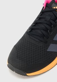 Czarny but sportowy z oddychającą siateczkową cholewką, różowym kołnierzem i pomarańczową podeszwą zewnętrzną, czarne sznurówki oraz fakturowane detale na czubku.