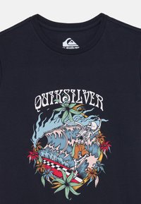 Navy blue cotton T-shirt featuring a colorful graphic of a skeleton surfing on a wave, surrounded by tropical plants and text.