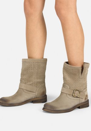 Bottines en daim beige avec une texture tissée, présentant une découpe en V sur le côté, une sangle avec une boucle métallique et un petit talon en bois.