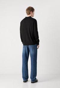 Schwarzer Strickpullover mit rundem Halsausschnitt und gerippten Bündchen, kombiniert mit locker sitzenden, hellblauen Jeans. Glatte Textur und lässiges Design.