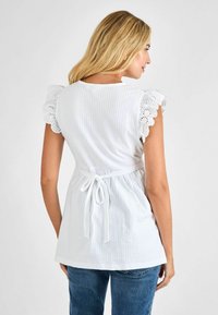 Weißes, strukturiertes Blusenshirt mit kurzen, Spitzendetails am Rand der Ärmel und einem gebundenen Taillengurt. Die Rückansicht zeigt das geraffte Design und das feine Streifenmuster.