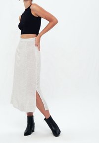Un crop top noir à côtelés associé à une jupe midi à motif argenté avec une fente sur le côté, portée avec des bottines noires. Design simple et moderne.