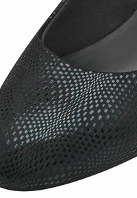 Svart sko med spetsig tå som har ett strukturerat, glänsande reptilskalig mönster på det övre materialet.