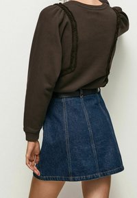 Sudadera marrón con mangas abullonadas, que presenta detalles texturizados a lo largo de las costuras. Combinada con una falda de mezclilla azul con costuras visibles.