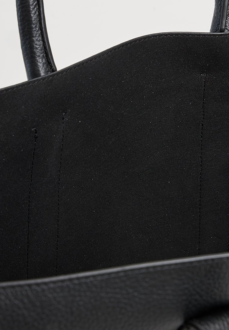 Innenseite einer schwarzen Ledertasche, die eine glatte Textur, minimale Nähte und ein offenes Design ohne sichtbare Taschen oder Fächer bietet.