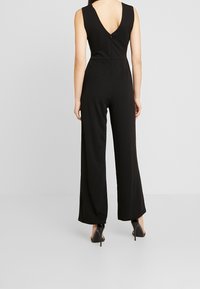 Mono negro sin mangas con un profundo escote en V en la parte posterior, diseño de pierna ancha y un detalle de cremallera oculta en la parte trasera. Textura de tela suave.