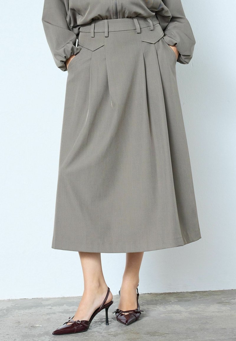 Gara, plīsvieta svārki gaiši pelēkā audumā ar augstu vidukli un jostas cilpām. Kombinēti ar tumši vīnsarkanām, ieapaļām slingbeka papēžiem.