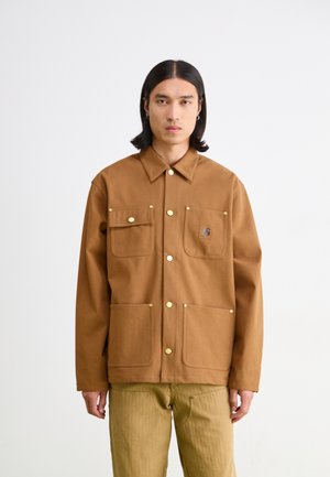 Brown cotton jacket with two chest pockets and two lower pockets, featuring gold-tone snap fasteners and a small embroidered logo.