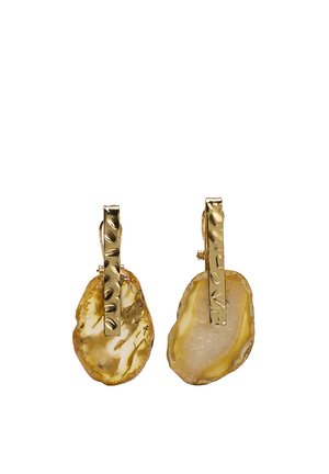 Złocone teksturowane kolczyki w kształcie pręta z nieregularnymi kroplami z bursztynowej żywicy, na klipsy, na białym tle.