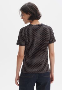 T-shirt marron à manches courtes avec un motif ondulé bleu marine, encolure ras du cou et coupe décontractée, associé à un jeans en denim foncé.