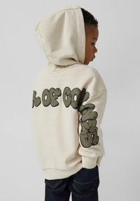 Beige hoodie met een grote, ronde grafische tekst op de achterkant en de linker mouw in donkergroen. Voorzien van een capuchon met trekkoord en ribgebreide manchetten.