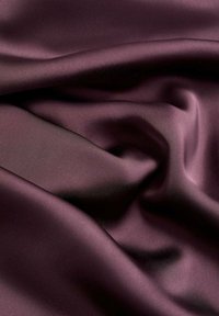 Burgundy satin fabric with a smooth, shiny texture, featuring soft folds and subtle variations in shade throughout the surface.